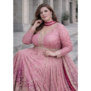Puede incluir: Un vestido rosa bordado con hilo dorado, de manga larga y escote en V. El vestido presenta detalles dorados y una gargantilla rosa a juego. El vestido es largo y tiene una falda fluida. La tela parece ser un material delicado y texturizado.