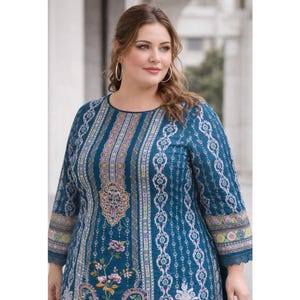 May include: A teal, long-sleeved dress with a round neckline. The dress features a detailed pattern with vertical stripes, floral accents, and decorative borders. The sleeves end just below the elbow. The dress is worn by a person.
