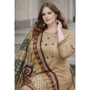 May include: A tan-colored, long-sleeved tunic and matching pants with a patterned shawl. The tunic features embroidered details around the neckline and sleeves. The shawl has a mix of green, burgundy, and gold patterns.