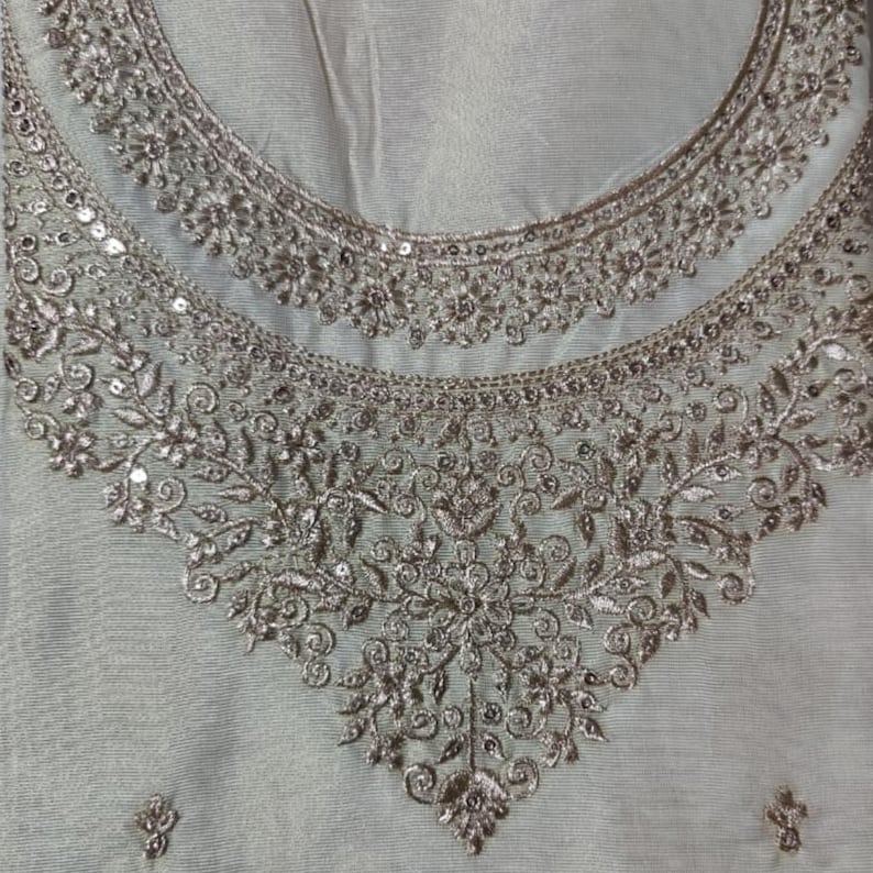 May include: A light gray fabric garment featuring an intricate neckline embellished with metallic silver embroidery and small reflective sequins. The embroidery forms a dense, symmetrical floral and vine pattern that extends downward in a V-shape.