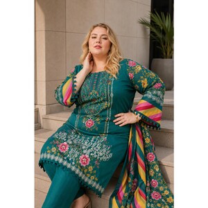May include: Teal-colored embroidered salwar kameez suit with floral patterns. The long-sleeved top features a square neckline and intricate white and pink floral embroidery. The suit includes matching pants and a patterned scarf.