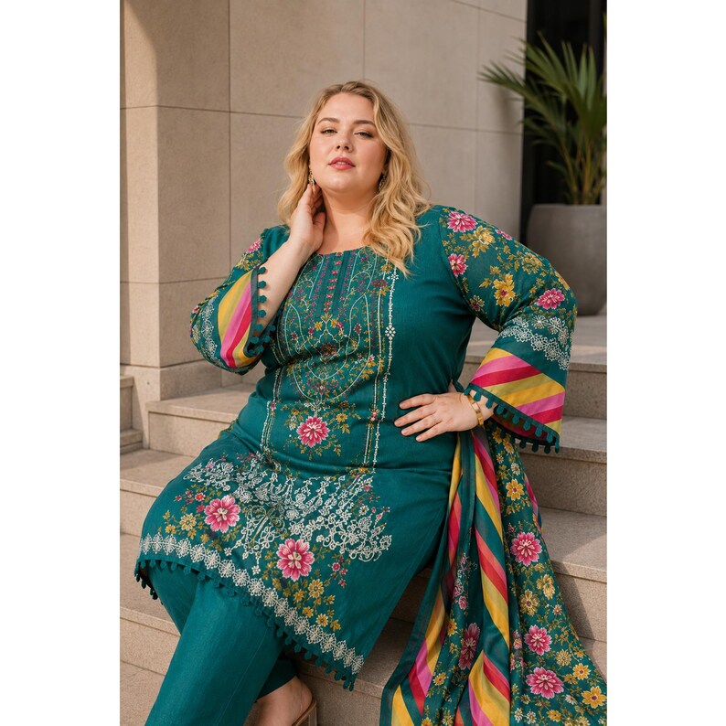 May include: Teal-colored embroidered salwar kameez suit with floral patterns. The long-sleeved top features a square neckline and intricate white and pink floral embroidery. The suit includes matching pants and a patterned scarf.