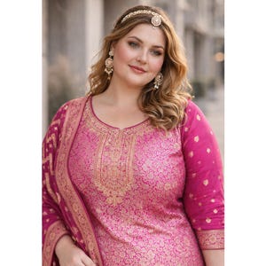 May include: A magenta-colored, embroidered Indian suit with gold accents. The suit features a detailed floral pattern and is paired with matching accessories, including a gold headpiece and earrings. The outfit is designed with a traditional aesthetic.