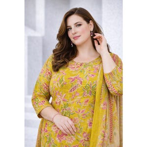 May include: A mustard yellow long-sleeved tunic featuring a repeating floral pattern in shades of pink, green, and white. The garment has a round neckline and is paired with a matching patterned scarf draped over the shoulder.