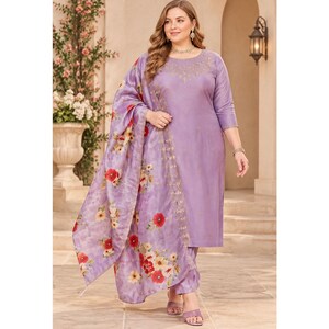 May include: A lavender-colored long-sleeved tunic and matching trousers set featuring delicate gold embroidery around the neckline. The outfit includes a coordinating lavender shawl adorned with a vibrant red and yellow floral print pattern.