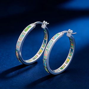 Puede incluir: Un par de pendientes de aro plateados con incrustaciones de ópalo de colores. Los pendientes tienen un cierre de bisagra. Las incrustaciones de ópalo presentan una mezcla de tonos verdes, amarillos y naranjas.