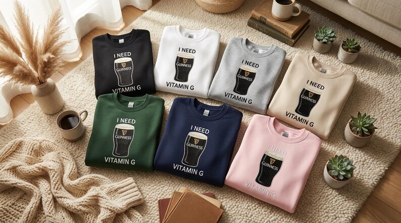 K&ouml;nnte beinhalten: Eine Auswahl an Sweatshirts mit Rundhalsausschnitt in verschiedenen Farben, darunter Schwarz, Wei&szlig;, Grau, Beige, Gr&uuml;n, Marineblau und Rosa. Jedes Sweatshirt zeigt eine Grafik eines Guinness-Pints mit dem Text "I NEED VITAMIN G".