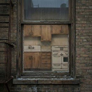 May include: A vintage kitchen scene viewed through a window. The kitchen features wooden cabinets, a white sink, a stove, and drawers. The window is framed by a weathered brick wall and a rusty fire escape.