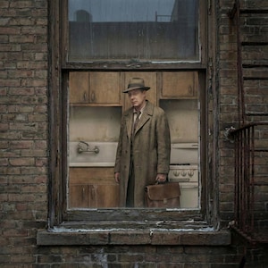 May include: A man in a brown overcoat and fedora stands inside a window frame, holding a briefcase. The window reveals a kitchen with wooden cabinets and a vintage stove. The scene is set against a brick wall.
