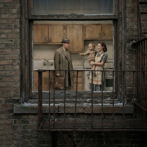 May include: A vintage-style photograph of a family in a kitchen, viewed through a window. A man in a hat and coat holds a briefcase, while a woman holds a child. The kitchen features wooden cabinets and a retro aesthetic. The scene is framed by a brick wall and a rusty metal balcony.