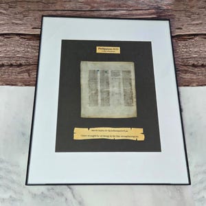 Puede incluir: Obra de arte enmarcada con un documento antiguo y texto. La obra incluye un passe-partout negro y un borde blanco dentro de un marco negro. El texto "Filipenses 4:13" es visible, junto con una cita en griego e ingl&eacute;s.