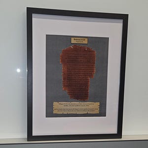 Puede incluir: Obra de arte enmarcada con un fragmento de texto antiguo. El texto es de color marr&oacute;n rojizo, montado sobre un fondo gris y enmarcado en negro. Se ven dos peque&ntilde;as placas con texto.