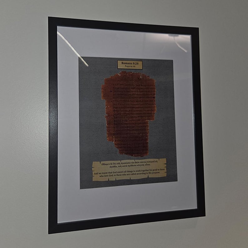 Puede incluir: Obra de arte enmarcada que presenta un fragmento de texto antiguo, probablemente un pasaje b&iacute;blico. El texto es de color marr&oacute;n oscuro, sobre un fondo gris, y est&aacute; enmarcado en negro. El marco incluye un paspart&uacute; blanco, realzando la presentaci&oacute;n de la obra.