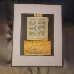 Puede incluir: Obra de arte enmarcada que presenta una p&aacute;gina de un texto religioso, con texto hebreo e ingl&eacute;s. La obra de arte se presenta en un marco blanco con un passe-partout negro. El texto es del Salmo 23, C&oacute;digos de Leningrado.