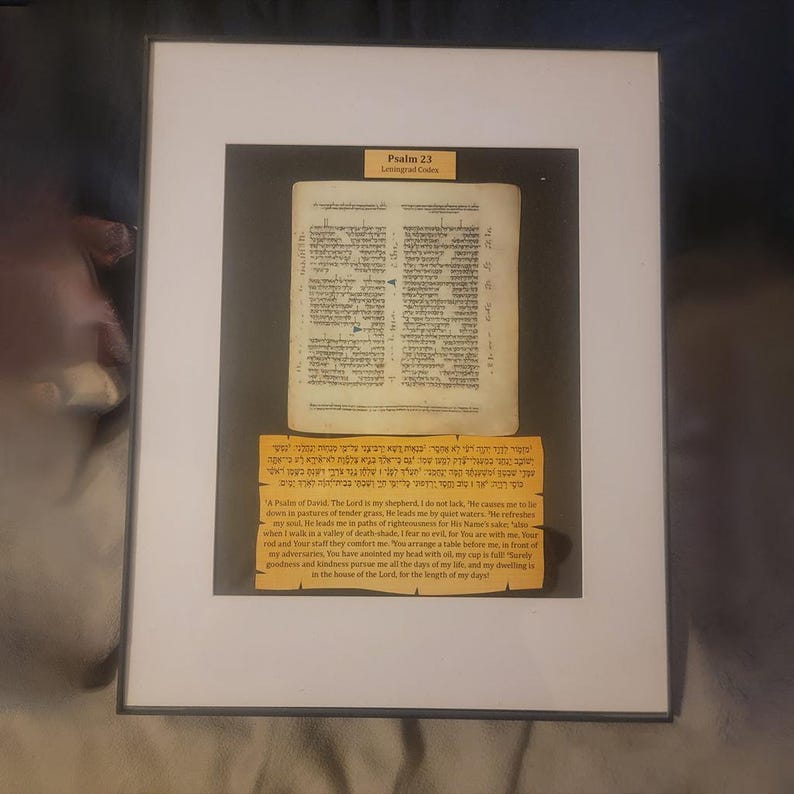 Puede incluir: Obra de arte enmarcada que presenta una p&aacute;gina de un texto religioso, con texto hebreo e ingl&eacute;s. La obra de arte se presenta en un marco blanco con un passe-partout negro. El texto es del Salmo 23, C&oacute;digos de Leningrado.