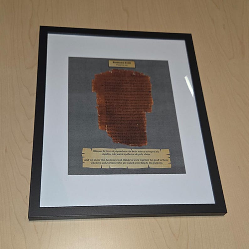 Puede incluir: Obra de arte enmarcada que presenta un fragmento de pergamino envejecido con texto. El pergamino marr&oacute;n est&aacute; montado sobre un fondo gris dentro de un passe-partout blanco. El marco negro rodea la obra, que incluye texto en la parte superior e inferior.