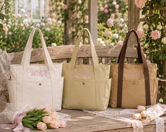May include: Three canvas tote bags with side pockets and a front pocket featuring a gold snap button. Each bag displays embroidered initials in pink thread: WRN on the white bag, QHX on the beige bag, and RLW on the tan bag with brown straps.