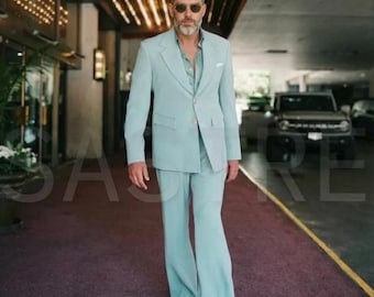 May include: A light blue suit with a matching jacket and flared pants. The suit is worn with a light blue shirt and dark sunglasses. The man is walking on a red carpet.