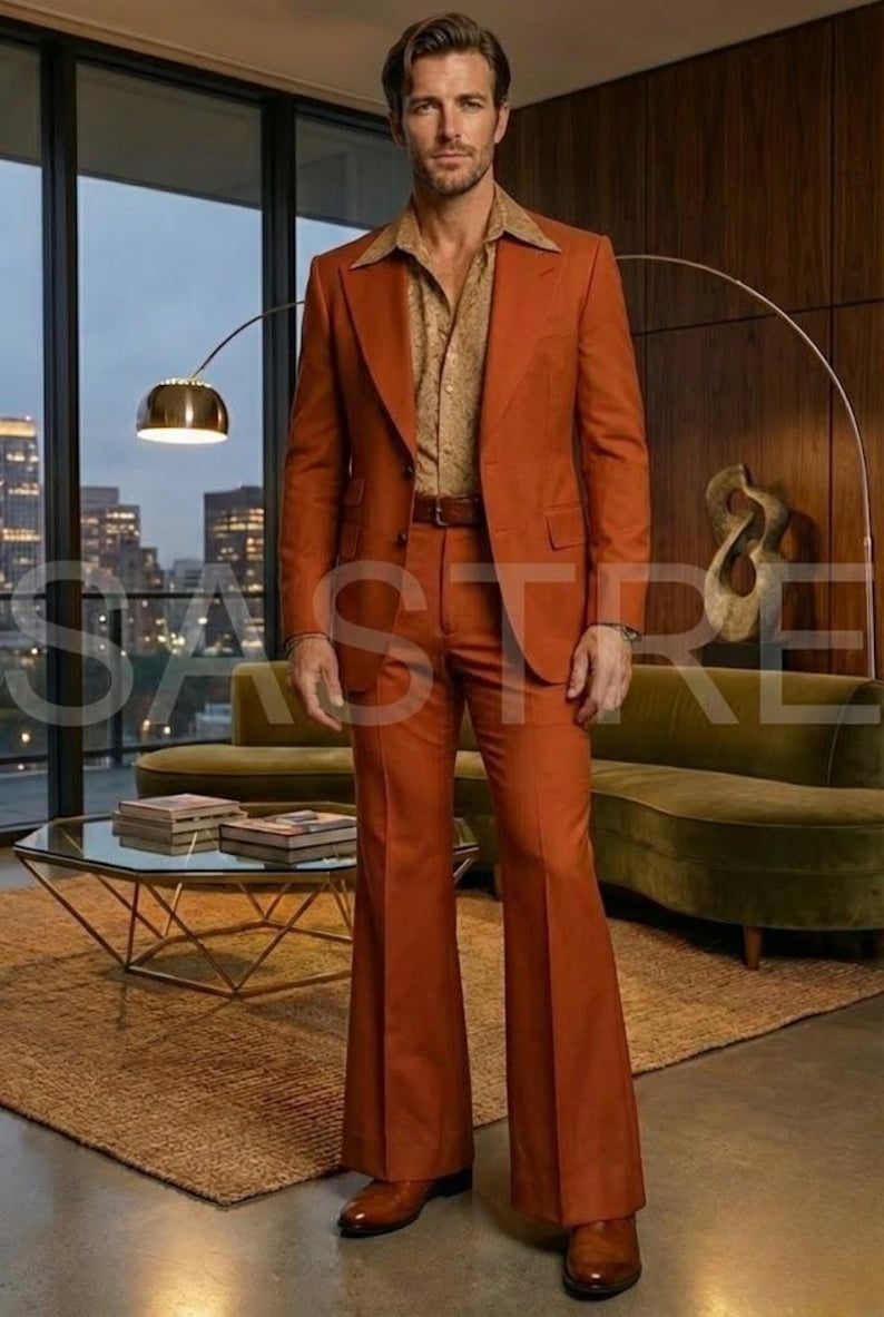 May include: A rust-colored suit with a wide lapel jacket and flared pants. The suit is paired with a patterned button-down shirt and a brown belt. The outfit is completed with brown leather shoes. The setting is a retro-style living room.