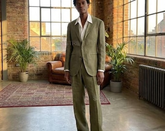 May include: A light green suit with a white collared shirt. The suit has a two-button jacket and matching trousers. The person is wearing brown suede loafers. The background includes a brick wall and large windows.