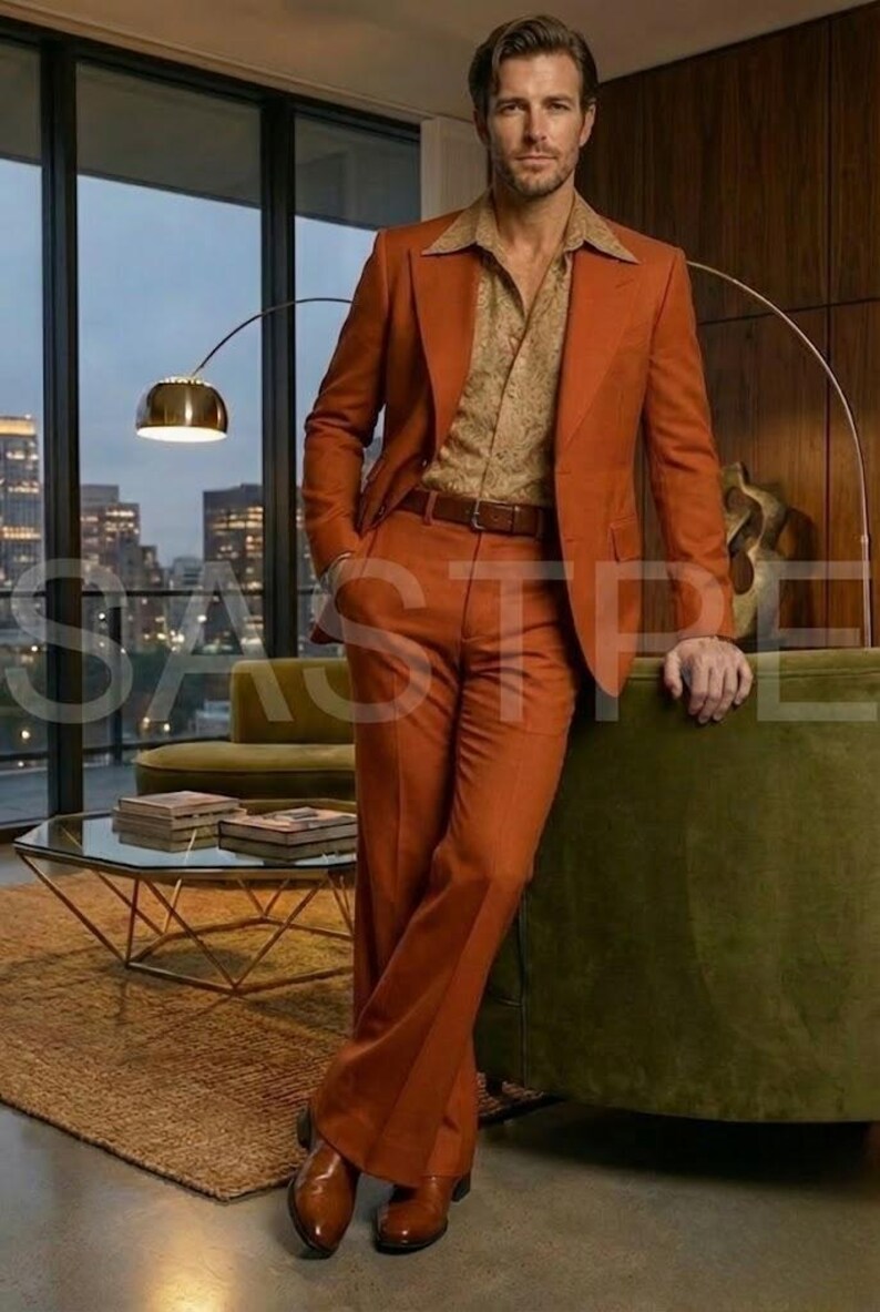 May include: A rust-colored suit with a matching jacket and wide-leg pants. The suit is paired with a patterned button-down shirt and a brown belt. The man is wearing brown leather shoes. The setting is a well-lit room with a city view.