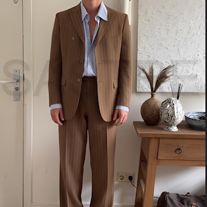 May include: A brown pinstripe suit with a light blue dress shirt. The suit includes a double-breasted blazer and matching wide-leg trousers. The person is wearing black sunglasses and black shoes.