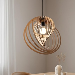 Könnte beinhalten: Eine Holz-Pendelleuchte mit einem einzigartigen, geschichteten Design hängt über einem Esstisch aus Holz. Die Leuchte hat eine Glühbirne in der Mitte und ist von konzentrischen Holzringen umgeben. Der Esstisch ist von Holzstühlen mit hellen Kissen umgeben.