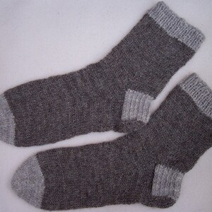 Könnte beinhalten: Zwei Paar graue und weiße Stricksocken. Die Socken haben einen grauen Körper und weiße Bündchen und Zehen.