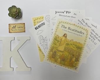 Puede incluir: Un conjunto de artículos religiosos, que incluyen un libro para colorear titulado "The Beatitudes", una letra decorativa de madera "K" y una pequeña suculenta. El libro presenta una ilustración de Jesús.