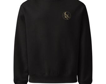May include: Black crew neck sweatshirt with a small gold emblem on the upper left chest. The emblem features a crescent moon, stars, and the letters "VK" in a circular design. The sweatshirt has long sleeves and a ribbed hem and cuffs.