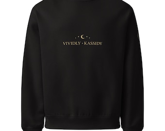 May include: Black crew neck sweatshirt with the text "VIVIDLY • KASSIDY" in gold lettering, along with a crescent moon and stars design. The sweatshirt has long sleeves and a ribbed neckline, cuffs, and hem.