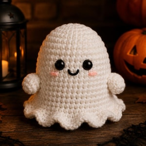 May include: A white crocheted ghost plush toy with a rounded head, small arms, and a ruffled base. It features two large black plastic safety eyes, a small embroidered black mouth, and two tiny pink stitched cheeks on its face.