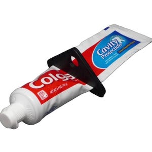Puede incluir: Un tubo de pasta dental Colgate rojo y blanco con un exprimidor de tubo de plástico negro. El tubo tiene el logotipo de Colgate y el sello ADA. El exprimidor ayuda a dispensar la pasta de dientes.