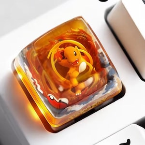 Peut inclure: Une touche de clavier mécanique carrée en résine translucide contenant un personnage Charmander orange. Le design présente des motifs de flammes orange et jaunes tourbillonnants, un petit détail de Poké Ball rouge et blanc et le mot Pokémon gravé.