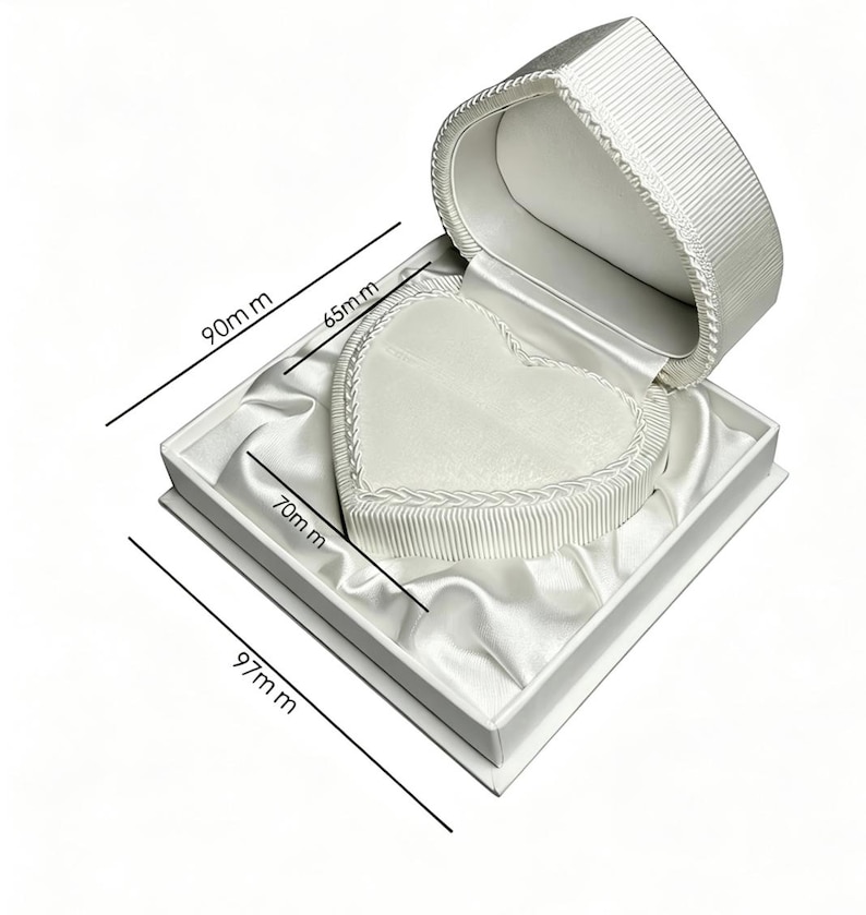 Pu&ograve; includere: Un portagioie bianco a forma di cuore con interno foderato in raso ed esterno a coste. La scatola presenta dimensioni di 90 mm per 97 mm, con un inserto interno a forma di cuore di 65 mm per 70 mm, indicate da linee di misurazione nere.