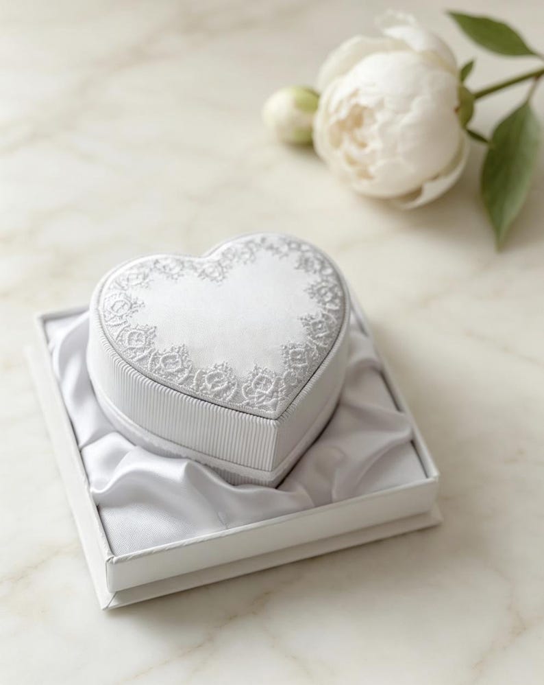 Pu&ograve; includere: Un portagioie bianco a forma di cuore con un lato a coste e un coperchio decorato con un intricato ricamo in pizzo bianco. La scatola &egrave; inserita all'interno di un contenitore di presentazione quadrato bianco foderato in morbido raso bianco.
