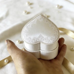 Pu&ograve; includere: Un portagioie a forma di cuore in raso bianco sporco con un delicato bordo in pizzo bianco lungo la parte superiore. I lati della scatola presentano una consistenza a coste e il coperchio &egrave; a forma di cuore per custodire piccoli gioielli.