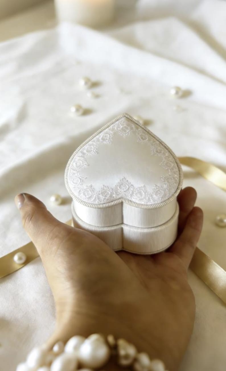Pu&ograve; includere: Un portagioie a forma di cuore in raso bianco sporco con un delicato bordo in pizzo bianco lungo la parte superiore. I lati della scatola presentano una consistenza a coste e il coperchio &egrave; a forma di cuore per custodire piccoli gioielli.