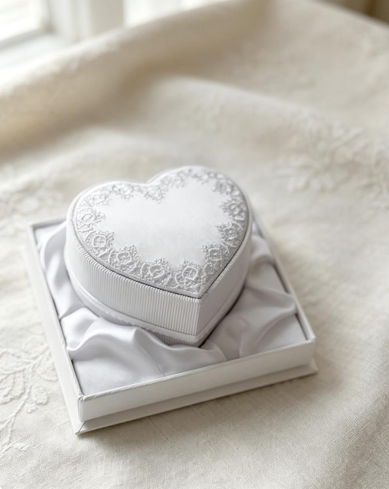 Pu&ograve; includere: Un portagioie bianco a forma di cuore con la parte superiore in raso decorata da un intricato ricamo in pizzo bianco lungo i bordi. I lati della scatola presentano una trama a coste ed &egrave; inserita in una scatola quadrata foderata in raso.