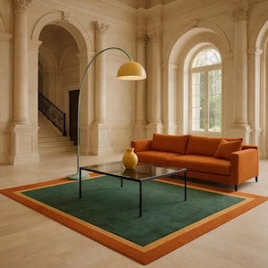 May include: An interior shot of a living room with an orange sofa, a green and orange rug, and a black coffee table. A yellow arched floor lamp and a yellow vase add pops of color. The room has large windows and columns.