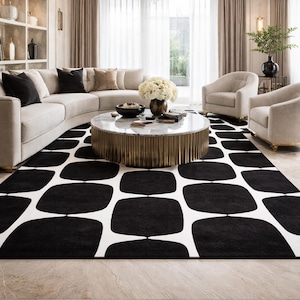 May include: A modern living room featuring a large black and white patterned rug. The rug is the focal point, with a repeating geometric design. A curved beige sofa, two armchairs, and a round coffee table complete the space. A chandelier hangs from the ceiling.