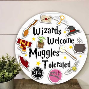 May include: A round white wooden sign with horizontal planks featuring the black text Wizards Welcome Muggles Tolerated. Illustrations include a broom, envelope, winged key, hat, scarf, mandrake, cauldron, wand, feather, 9 3/4 sign, and cake.