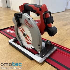 Op de afbeelding: Een rode en zwarte Milwaukee cirkelzaag met een zilveren zaagblad, op een rood en zwart spoor. De zaag heeft een zwarte handgreep en het Milwaukee-logo is zichtbaar. Ontworpen voor het zagen van hout en andere materialen.