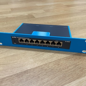Op de afbeelding: Een blauwe netwerkswitch met acht poorten, genummerd van 1 tot 8, en de tekst "tp-link 8-Port Gigabit Desktop Switch". Het apparaat is gemonteerd in een blauwe rack.