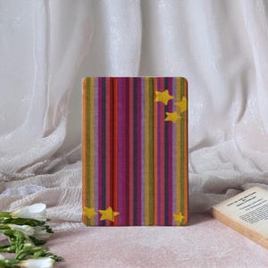 Peut inclure: Un étui rectangulaire avec un motif rayé coloré dans les tons de rose, violet, jaune et orange. L'étui est orné de plusieurs étoiles jaunes. L'étui est probablement pour une tablette ou une liseuse.