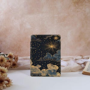 May include: A rectangular case with a celestial design. The navy blue background is adorned with a gold sun, stars, and clouds. The case has a glossy finish, possibly for an e-reader or tablet. The design has a mystical or astrological theme.