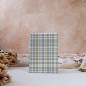 May include: A rectangular e-reader case featuring a plaid pattern in shades of light green, soft blue, and white. The case has a smooth, flat surface with a grid of intersecting horizontal and vertical lines forming a classic tartan design.