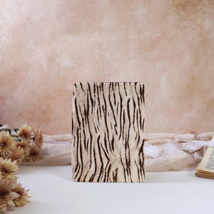 May include: A rectangular decorative box with a cream-colored background and dark brown vertical stripe pattern. The box is standing upright on a white surface, with a soft pink background.