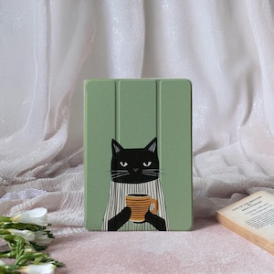 Könnte beinhalten: Eine grüne Tablet-Hülle mit einer Illustration einer schwarzen Katze. Die Katze trägt ein gestreiftes Hemd und hält einen gestreiften orange-braunen Becher. Die Hülle hat ein dreifaches Design.