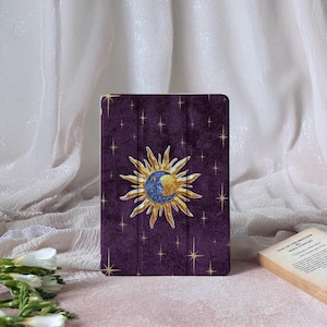 May include: A purple tablet case featuring a celestial design. The design includes a gold sun and moon with a starry background. The case is rectangular and has a textured appearance.